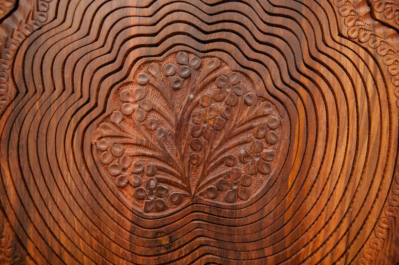 May include: Close-up of a wooden decorative bowl with a carved floral design. The bowl has a warm brown color and a wavy, layered pattern. The floral carving is in the center, adding a touch of elegance to the wooden bowl.