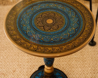 May include: A round side table with a decorative, hand-painted design. The tabletop features a central floral motif in blue and gold, surrounded by intricate patterns. The table has a pedestal base and measures approximately 50 cm in diameter.