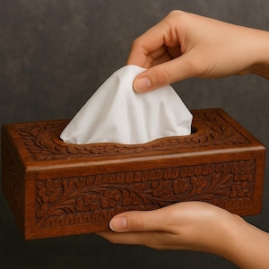 以下が含まれることがあります： 茶色の長方形の木製ティッシュボックス。精巧な花の彫刻が施されています。白いティッシュが見えます。手はティッシュを取り出そうとしています。木材は暖色です。