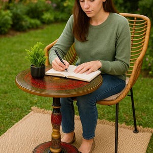 May include: A round, decorative side table with a detailed, colorful design. The table has a red and green pattern on the top and base, with a black and gold central support. A small potted plant sits on the table.
