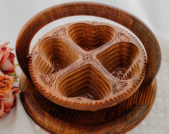 May include: A decorative wooden serving basket with a round base and a handle. The basket features a heart-shaped design with intricate carvings and a natural wood finish. The handle is also carved with a decorative pattern.