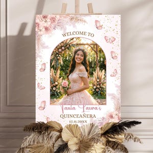 Peut inclure: Panneau de bienvenue pour une quinceañera, avec une photo d'une jeune femme en robe rose. Le panneau affiche "Bienvenue à Tania Laura's Quinceañera" et la date 12.11.20XX, avec des motifs floraux et papillons.