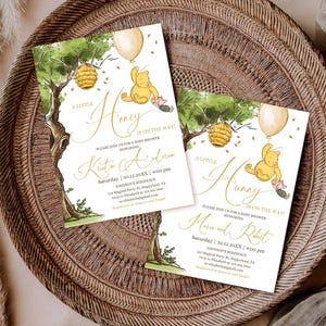 May include: Two baby shower invitations with a Winnie the Pooh theme. The invitations feature illustrations of Winnie the Pooh, a tree, a beehive, and a balloon. The text reads "A Little Honey is on the Way!" and includes the honoree's name, date, time, and location.