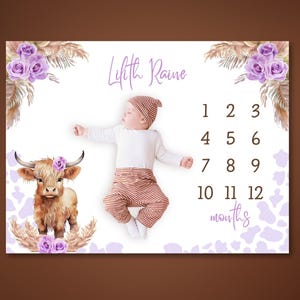 May include: A white milestone blanket with a watercolor illustration of a Highland cow and floral accents. The blanket includes the name "Lilith Raine" and numbers for tracking baby's age in months.
