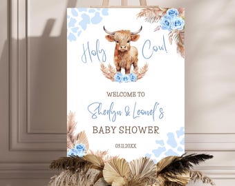 May include: A baby shower sign with the text "Holy Cow!" and "Welcome to Sherlyn & Leonel's Baby Shower." The sign features a watercolor illustration of a Highland cow, blue flowers, and cow print accents. The date is 03.11.20XX.