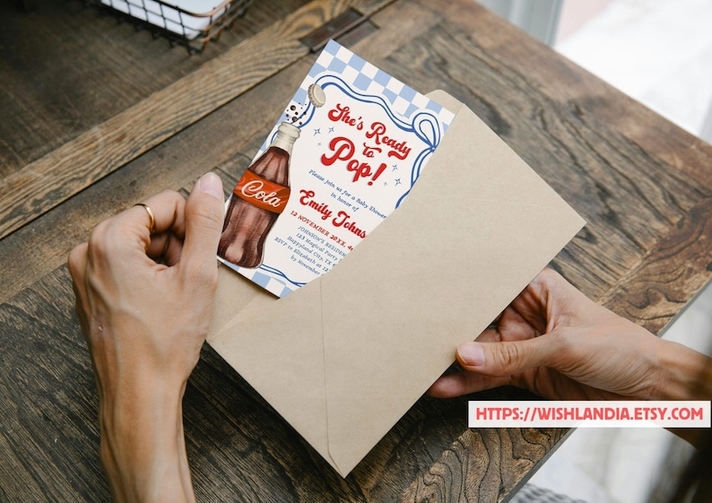 Puede incluir: Una invitaci&oacute;n para baby shower con una ilustraci&oacute;n de botella de cola de estilo vintage. La invitaci&oacute;n dice "She's Ready to Pop!" en escritura roja, con detalles del evento para Emily Johns. La invitaci&oacute;n est&aacute; en un sobre beige.