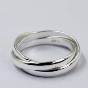 Könnte beinhalten: Ein silberner Ring mit drei ineinandergreifenden Bändern. Die Bänder sind glatt und poliert und reflektieren das Licht. Der Ring ist vor einem schlichten weißen Hintergrund platziert, was seine schlichte Eleganz unterstreicht. Dieser Schmuck eignet sich für den Alltag.