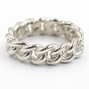 Può includere: Un anello color argento con un design a catena. L'anello è realizzato in metallo lucido e presenta un motivo continuo e ad incastro. L'anello è mostrato su sfondo bianco.
