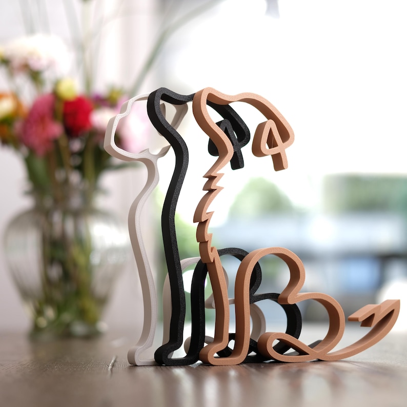 K&ouml;nnte beinhalten: Eine Holzskulptur eines Hundes in drei Farben: Wei&szlig;, Schwarz und Hellbraun. Die Skulptur ist eine stilisierte Umrisszeichnung eines Hundes, wobei der K&ouml;rper und der Kopf durch den negativen Raum gebildet werden. Der Hund sitzt auf einer Holzoberfl&auml;che.