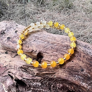 May include: A multi-strand wrap bracelet featuring translucent yellow and orange spherical beads interspersed with small metallic gold spacers. The circular jewelry piece is constructed with a flexible wire frame that maintains its coiled shape.