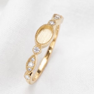 Könnte beinhalten: Ein goldener Ring mit einer zentralen ovalen Fassung mit texturierter Basis, flankiert von kleinen runden und marquiseförmigen klaren Steinen. Das Band weist ein feines Perlenranddetail um die Steine und die zentrale ovale Fassung auf.