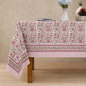 May include: A rectangular tablecloth featuring a repeating floral pattern in shades of pink and green on a cream background. The fabric has a wide border with a smaller floral vine motif and a thin striped edge in light pink and white.