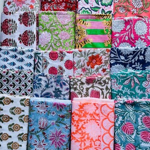 May include: A selection of folded fabric squares displaying diverse floral patterns. The fabrics showcase a spectrum of colours, such as pink, red, green, blue, and orange, with intricate botanical designs. The textiles are neatly stacked, highlighting the variety of prints.