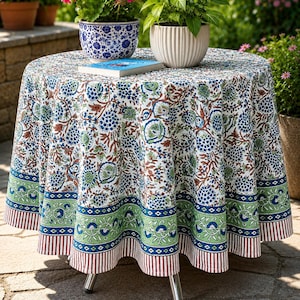 May include: A round tablecloth featuring a white base with a dense floral pattern in blue, green, and brown. The border includes a green band with blue floral motifs, a geometric diamond trim, and a bottom edge with vertical brown and white stripes.