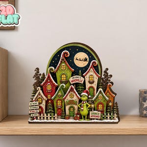 Könnte beinhalten: Ein dekoratives Holzdisplay mit einer Whoville-Dorfszene, bunten Häusern, einer Grinch-Figur und einem Nachthimmel mit Mond und Schlittensilhouette. Die Schilder tragen die Aufschriften Welcome to Whoville, Be Merry, Be Grinchy, Be Who-You, Be Kind und Grinch Approved.