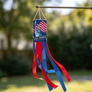 May include: A patriotic windsock featuring the Statue of Liberty and the American flag, with the text "JULY FOURTH." The windsock has red, white, and blue streamers, perfect for Independence Day celebrations.