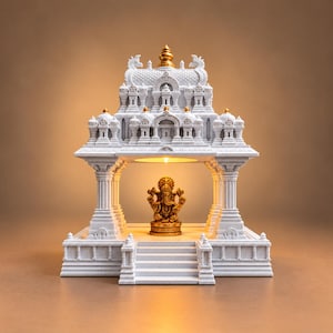 May include: A white temple structure with intricate architectural details and gold accents, featuring a central illuminated alcove. Inside the alcove sits a small, gold-colored Ganesha figurine on a pedestal, positioned at the top of a set of stairs.