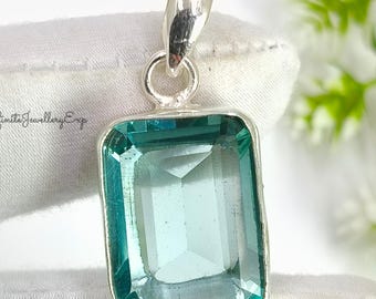 May include: A rectangular, teal-colored gemstone pendant with a silver setting. The pendant has a rectangular shape with a faceted surface. The bail is silver and attached to the top of the pendant. The text "Infinita Jewellery Exp" is visible.