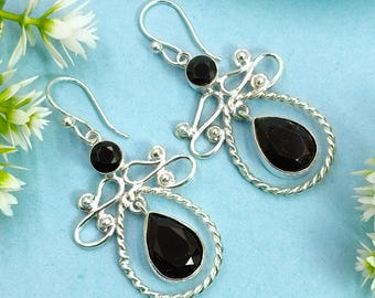 May include: A pair of silver earrings with black gemstones. Each earring features a round black stone at the top and a teardrop-shaped black stone within a twisted silver frame. The earrings have a hook closure.