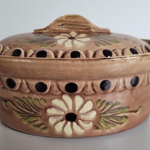 Puede incluir: Una fuente de cerámica marrón con tapa. La fuente presenta diseños florales en crema y verde, con detalles en negro. La tapa tiene un asa decorativa y orificios de ventilación. Capacidad aproximada de 2 litros.
