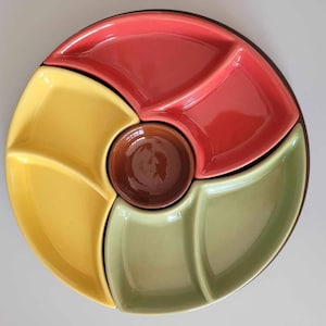 May include: A colorful ceramic serving platter with four sections in red, yellow, and green, plus a central brown dip bowl. The round platter has a dark brown rim and is ideal for serving snacks or appetizers.