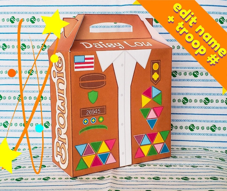 May include: A brown cardboard box with a Girl Scout Brownie troop logo. The box is decorated with a vest design, including a US flag, a badge, and a troop number 26945. The text "Daisy Lou" is printed on the box.