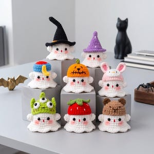 May include: A collection of eight small, white, crocheted ghost figures, each wearing a different colorful hat. The hats include a black witch hat, a purple wizard hat, a blue cap, an orange pumpkin, pink bunny ears, a green alien, a red strawberry, and a brown bear cap.