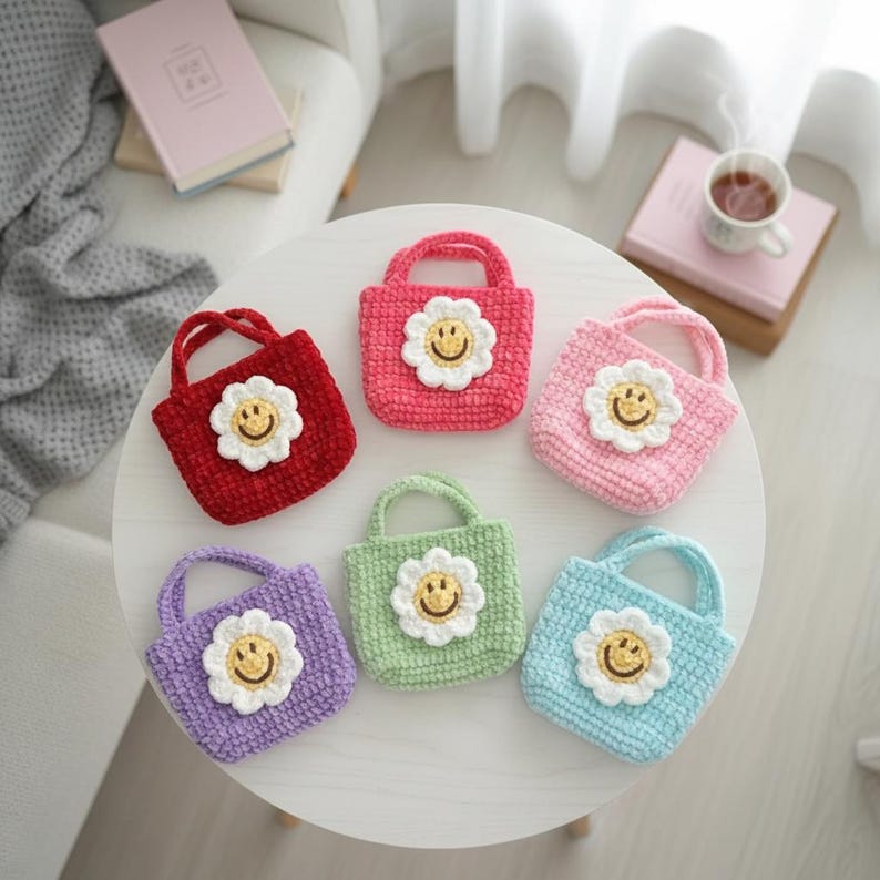 K&ouml;nnte beinhalten: Sechs kleine, geh&auml;kelte Tragetaschen in verschiedenen Farben: Rot, Rosa, Hellrosa, Gr&uuml;n, Lila und Blau. Jede Tasche hat eine wei&szlig;e G&auml;nsebl&uuml;mchen-Applikation mit gelbem Smiley-Gesicht. Die Taschen haben kleine Griffe.