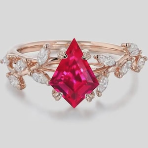 Op de afbeelding: Een roségouden ring met een opvallende, vlieger-vormige rode edelsteen als middelpunt. De ring is versierd met delicate bladeren en marquise-geslepen witte edelstenen, wat een elegant, door de natuur geïnspireerd ontwerp creëert. Een prachtig sieraad.