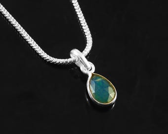 May include: A silver necklace with a teardrop-shaped pendant. The pendant features a faceted, blue-green gemstone set in a gold-colored bezel. The chain is a delicate, textured design.