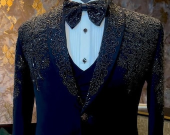 Puede incluir: Un traje formal azul marino exhibido en un maniquí. El traje presenta intrincados adornos de cuentas en las solapas y los hombros. Incluye una pajarita a juego, una camisa blanca y un chaleco. El traje está confeccionado con un cierre de un solo botón.