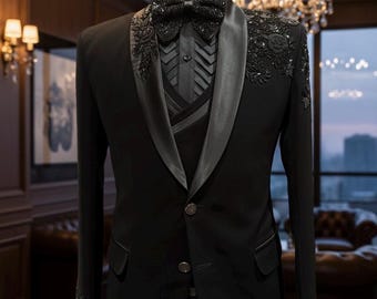 May include: A formal black suit displayed on a mannequin. The suit features a satin lapel, a matching bow tie, and intricate beaded embellishments on the shoulders and sleeves. The suit includes a vest and a dress shirt with a pleated design.
