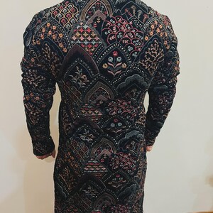 May include: A black long-sleeve jacket with intricate embroidery in shades of red, pink, gold, and green. The jacket features a detailed pattern of floral and geometric designs, creating a rich, textured appearance. The garment is likely made of a velvet or similar fabric.