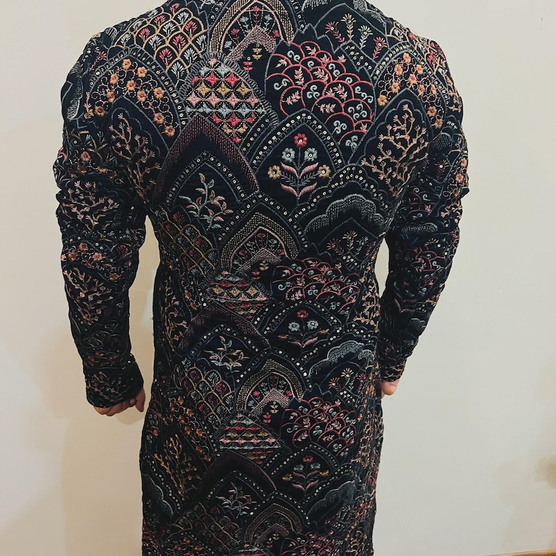 May include: A black long-sleeve jacket with intricate embroidery in shades of red, pink, gold, and green. The jacket features a detailed pattern of floral and geometric designs, creating a rich, textured appearance. The garment is likely made of a velvet or similar fabric.