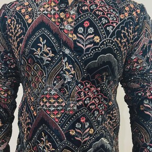 May include: A dark navy blue jacket with intricate embroidery in shades of pink, gold, and cream. The jacket features a mandarin collar and button closure. The detailed floral and geometric patterns cover the entire garment, creating a rich, textured appearance.