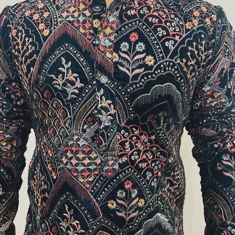 May include: A dark navy blue jacket with intricate embroidery in shades of pink, gold, and cream. The jacket features a mandarin collar and button closure. The detailed floral and geometric patterns cover the entire garment, creating a rich, textured appearance.