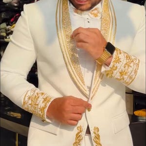 May include: A white suit with gold embroidery. The suit features intricate gold detailing on the lapels, cuffs, and along the jacket's edges. The ensemble includes a matching bow tie and is a formal wear item.