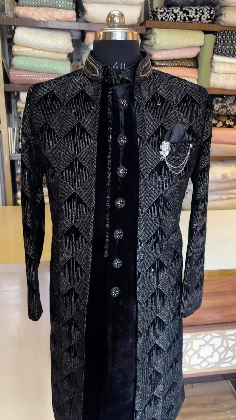 Peut inclure: Veste de c&eacute;r&eacute;monie noire avec un motif g&eacute;om&eacute;trique. La veste pr&eacute;sente un col officier, des boutons d&eacute;coratifs et une pochette avec une &eacute;pingle d&eacute;corative. La veste est pr&eacute;sent&eacute;e sur un mannequin.