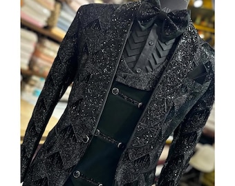 May include: A formal black suit with a textured, sparkling pattern. The suit includes a double-breasted vest, a long-sleeved jacket, and a bow tie. The suit is displayed on a mannequin.