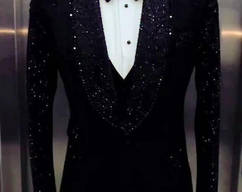 Puede incluir: Un esmoquin negro con cuello chal y solapas con lentejuelas. El traje formal incluye una camisa blanca, una pajarita negra y un chaleco negro. El traje está hecho a medida para eventos especiales.