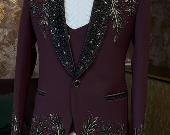 Puede incluir: Traje de tres piezas burdeos con intrincados diseños florales de cuentas negras y plateadas. El traje incluye una americana, un chaleco y una pajarita. Las solapas y los puños están adornados con abalorios detallados. Se ve una camisa blanca.