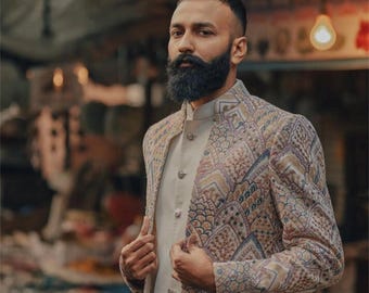 May include: A patterned jacket with a mandarin collar and a light-colored shirt. The jacket features a detailed geometric design in shades of brown, blue, and beige. The outfit is suitable for formal occasions.