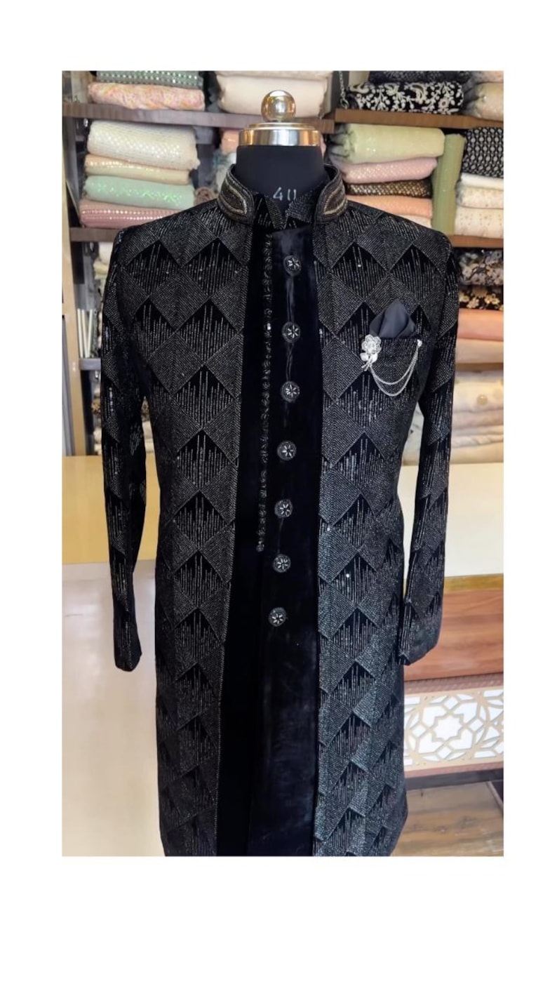 Peut inclure: Veste de c&eacute;r&eacute;monie noire avec un motif g&eacute;om&eacute;trique et un panneau de velours sur le devant. La veste pr&eacute;sente un col mandarin, des boutons d&eacute;coratifs et une pochette avec une cha&icirc;ne. La veste est pr&eacute;sent&eacute;e sur un mannequin.