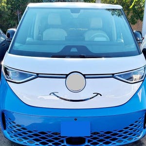 May include: A blue and white electric van with a smiling face design on the front. The van has a blue front bumper and a white upper body. The windshield is large, and the headlights are sleek and modern.