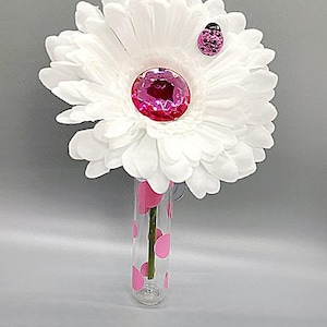 May include: A white gerbera daisy with a pink rhinestone center and a pink ladybug accent is displayed in a clear glass vase with pink polka dots.