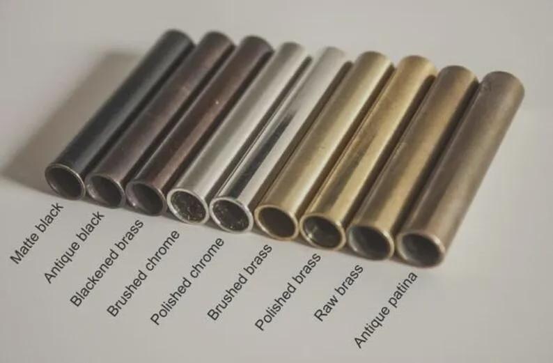 Pode incluir: Uma cole&ccedil;&atilde;o de tubos de metal em v&aacute;rios acabamentos, incluindo preto fosco, preto antigo e cromo polido. A imagem exibe uma gama de cores do escuro ao claro, com etiquetas que identificam cada acabamento. Os tubos est&atilde;o dispostos diagonalmente.