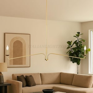 Puede incluir: Una lámpara de araña moderna, dorada, con dos luces horizontales. La lámpara está suspendida del techo e ilumina una sala de estar con un sofá seccional beige, una mesa de centro redonda y una obra de arte enmarcada.