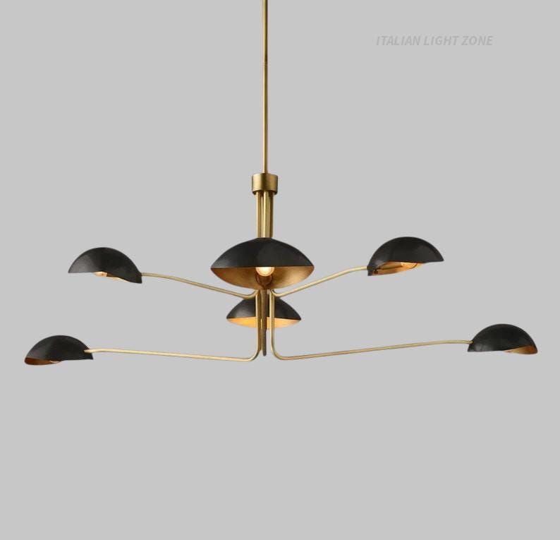 Pode incluir: Um candelabro moderno com acabamento dourado e abajures pretos. A lumin&aacute;ria possui um cubo central com v&aacute;rios bra&ccedil;os que se estendem para fora, cada um segurando uma luz preta em forma de c&uacute;pula. O texto "ITALIAN LIGHT ZONE" &eacute; vis&iacute;vel.