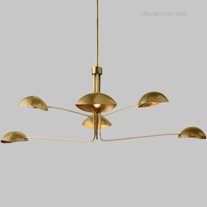 Pode incluir: Um lustre moderno em lat&atilde;o com seis bra&ccedil;os curvos, cada um com uma lumin&aacute;ria em forma de c&uacute;pula. A lumin&aacute;ria central tem um design semelhante, com um brilho quente emanando das l&acirc;mpadas. O texto "ITALIAN LIGHT ZONE" &eacute; vis&iacute;vel.
