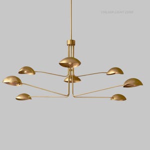 Pode incluir: Um lustre moderno em tom dourado com v&aacute;rios bra&ccedil;os curvos, cada um com uma lumin&aacute;ria em forma de c&uacute;pula. A lumin&aacute;ria tem uma coluna central e o texto "ITALIAN LIGHT ZONE".